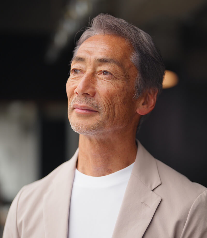 Middle-aged man with gray hair wearing a light jacket, looking thoughtfully ahead.