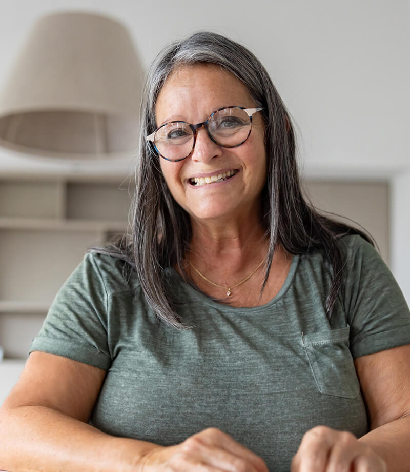 Smiling middle-aged woman wearing glasses and a green shirt indoors.