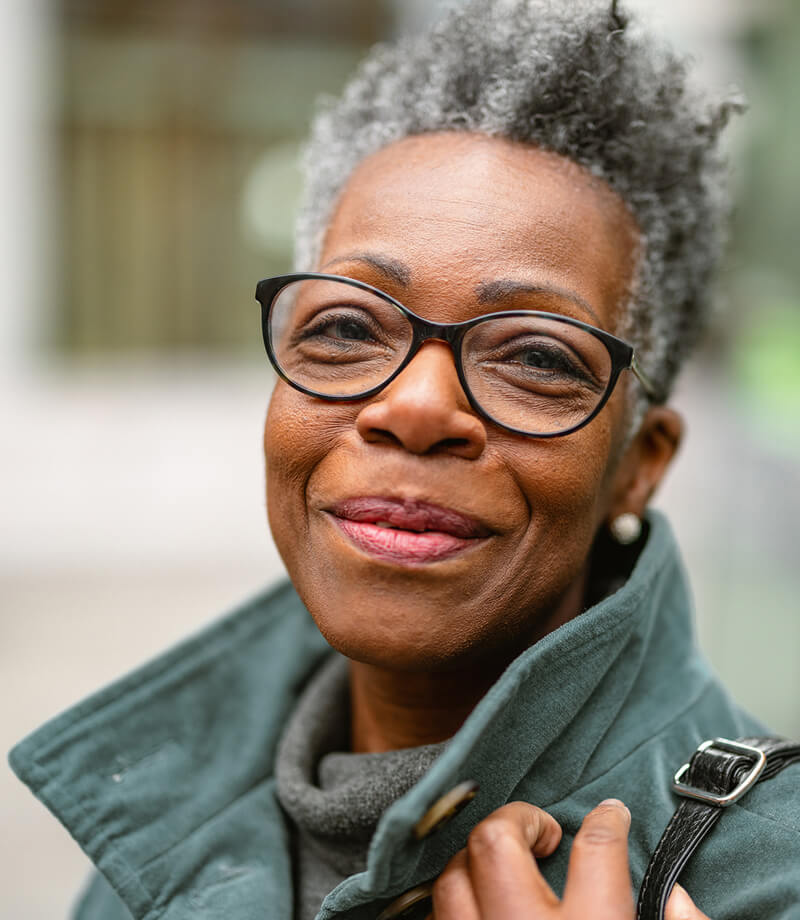 Smiling older woman with short gray hair wearing glasses and a green coat.